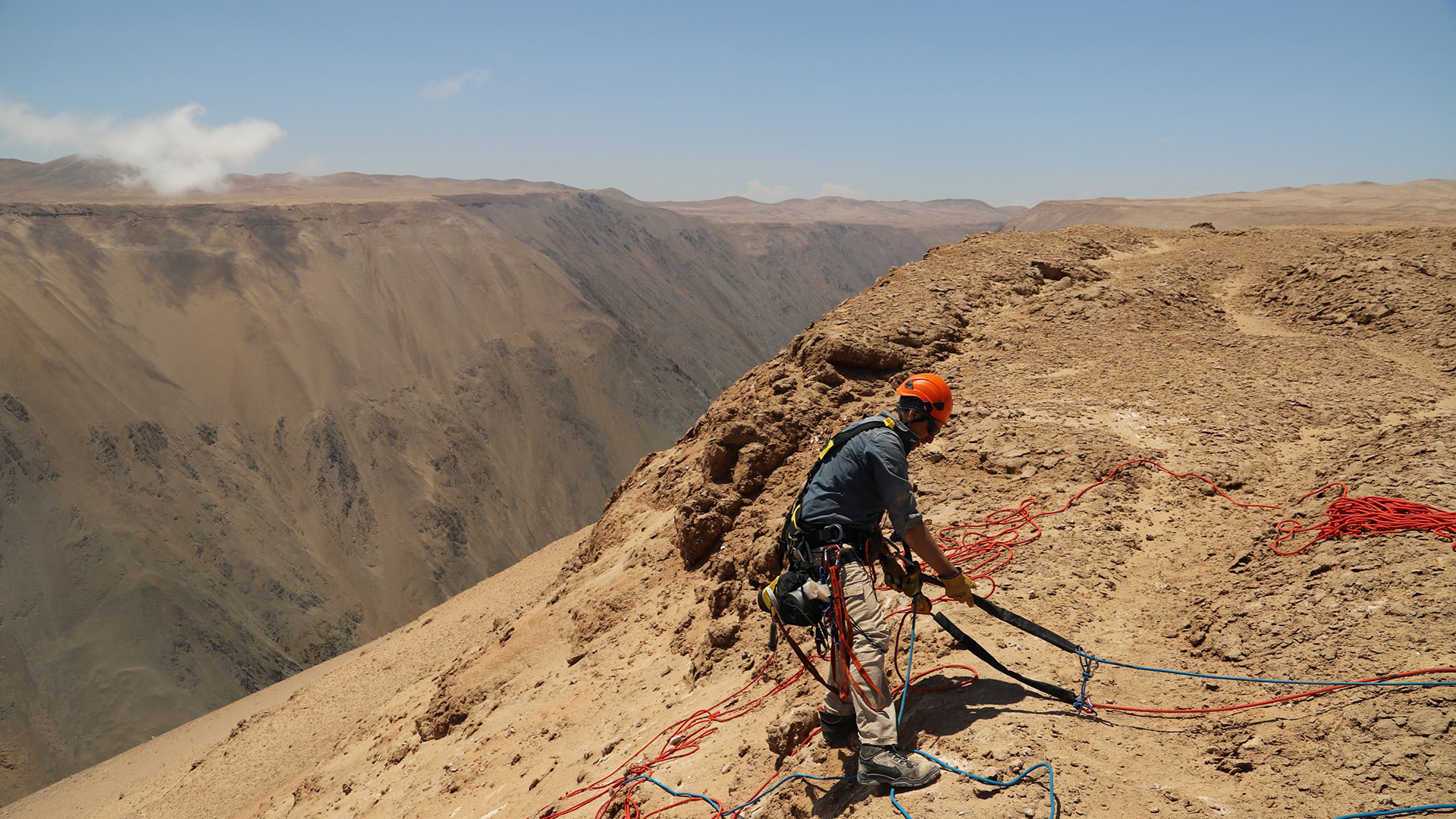 Shots from research happening in the desert, like a truck kicking up dust or a person climbing with rope down the side of a cliff.
