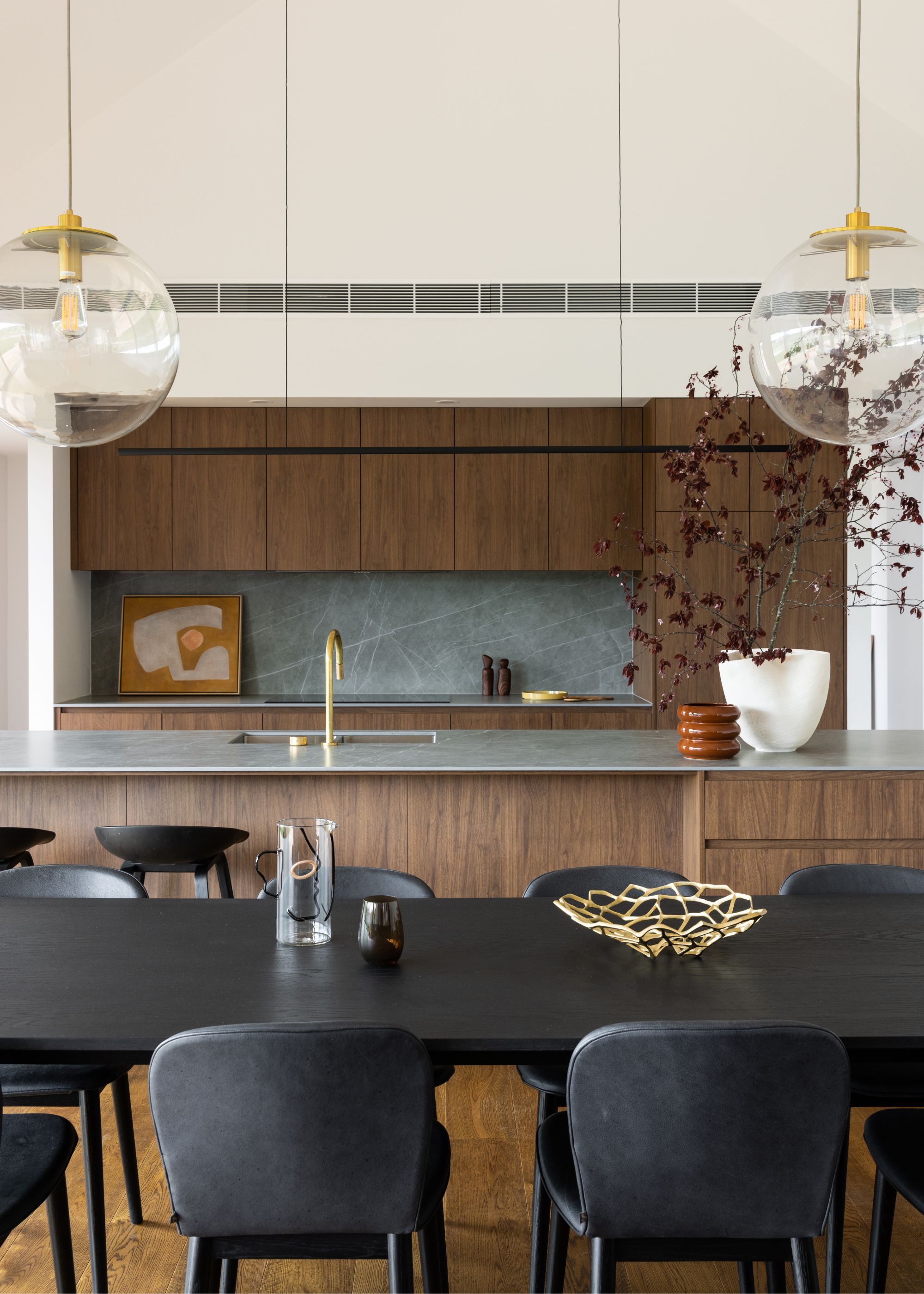 A slender kitchen countertop on an island with pendant lights hanging above. There is also a dining table with a gold bowl in the middle.