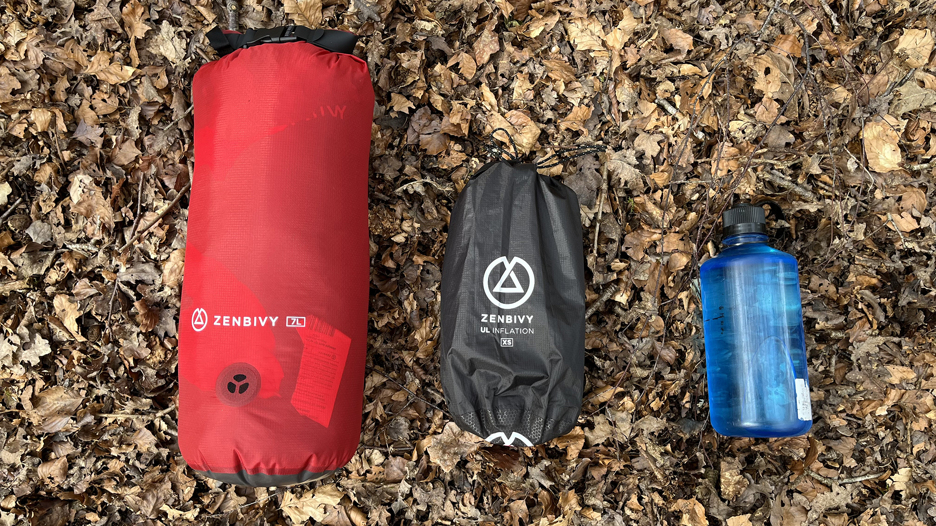 A Zenbivy stuff sack, uninflated mattress and water bottle on a floor of fallen leaves.