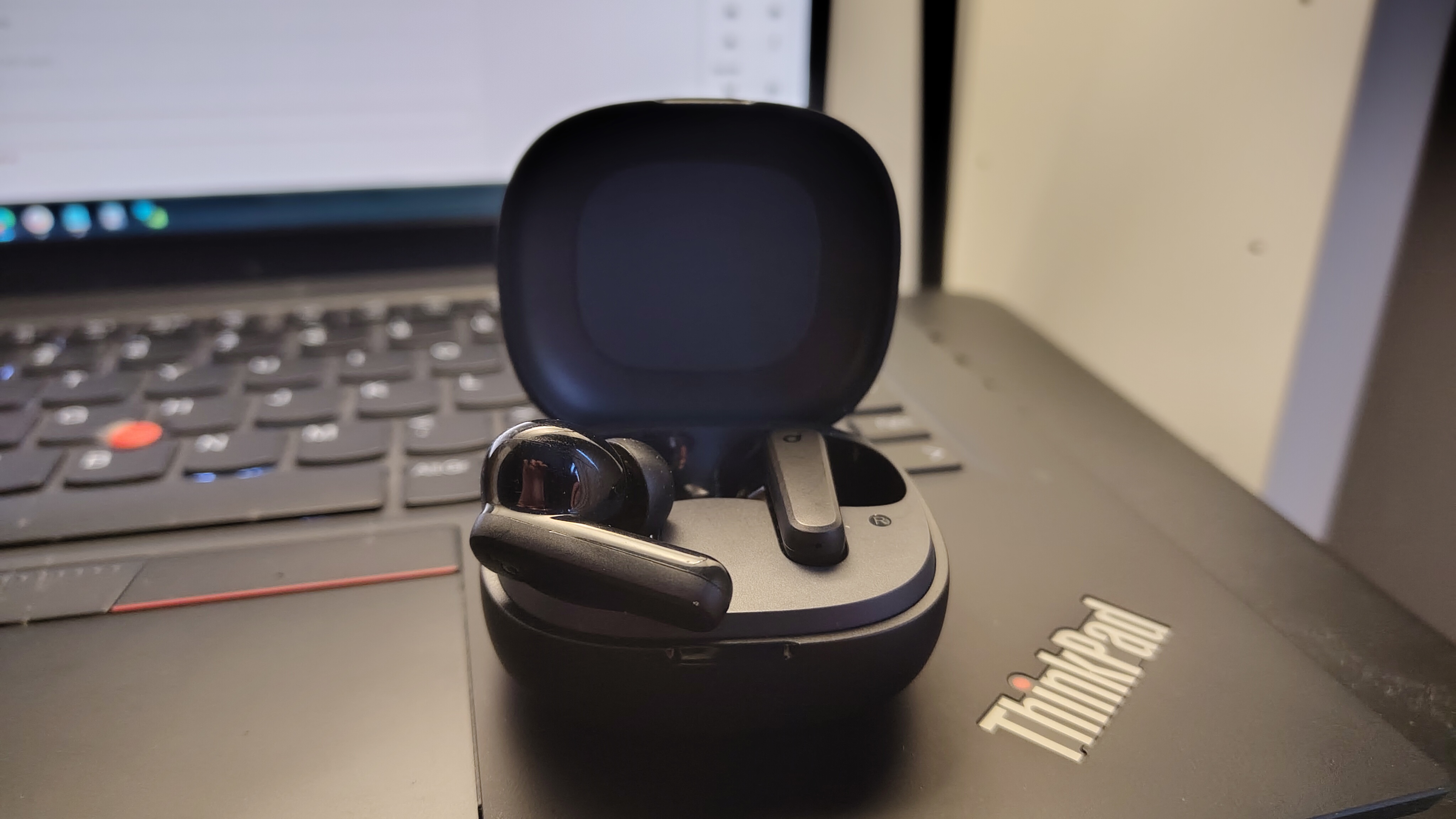 A pair of Anker SoundCore P20i earbuds in an open case sitting on a ThinkPad