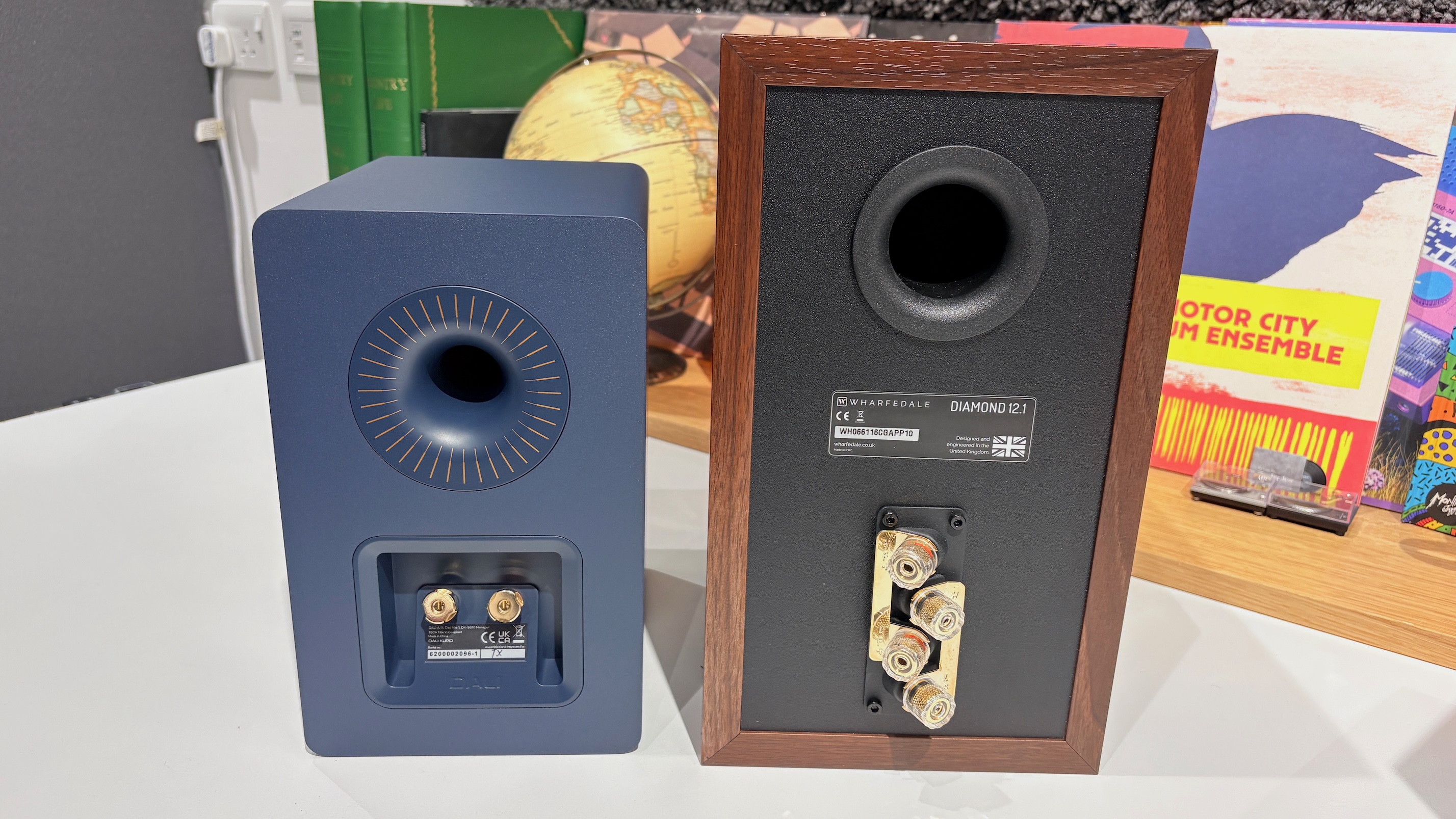 A Dali Kupid and a Wharfedale Diamond 12.1 speaker shot from behind to show their connections. In the background are vinyl album covers.