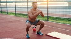 Man performing a squat outdoors next to exercise mat and kettlebell