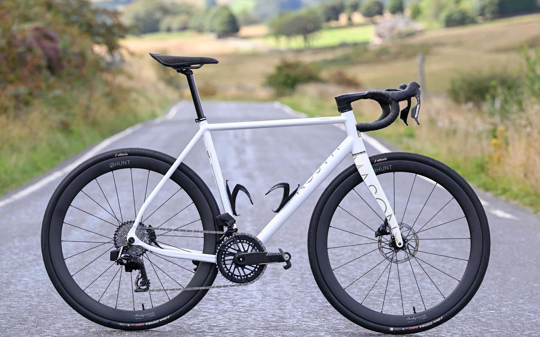 a white bike with carbon rims and a black saddle side on in the middle of a country lane