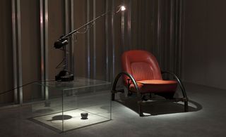 Black table lamp with a long arm, shining onto a red leather chair