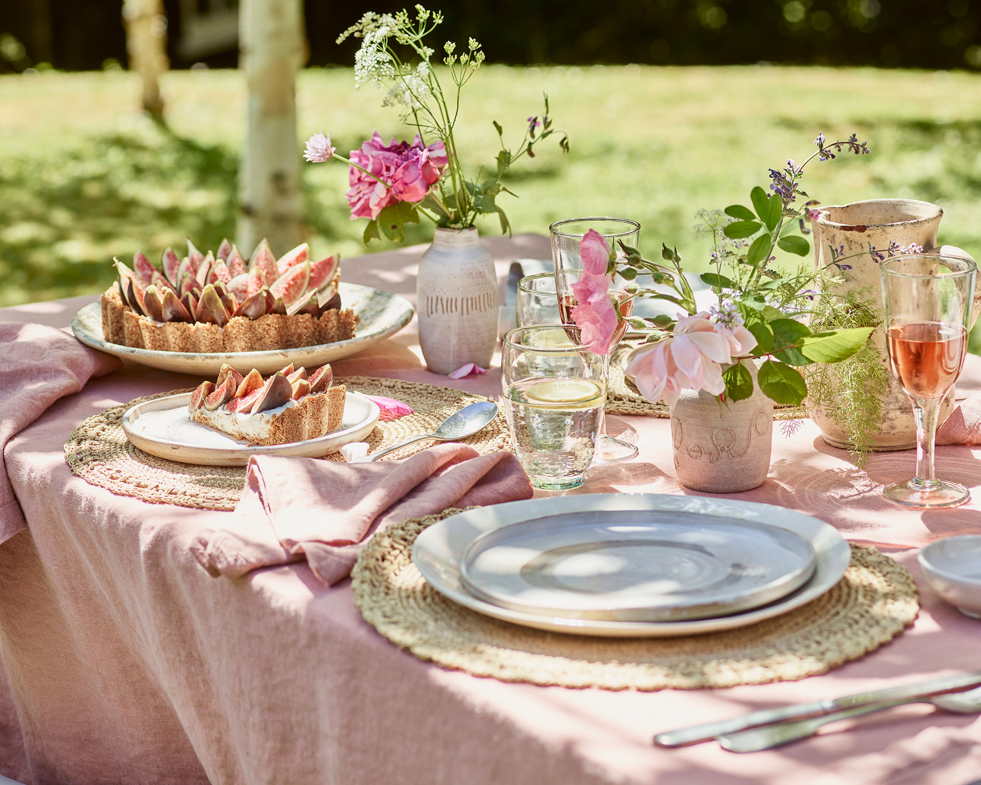 Summer table setting with pink tablecoth, napinks and summer food and woven placemats