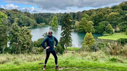 Kathryn Williams poses in front of a lake surrounded by leafy trees and grass on a walk