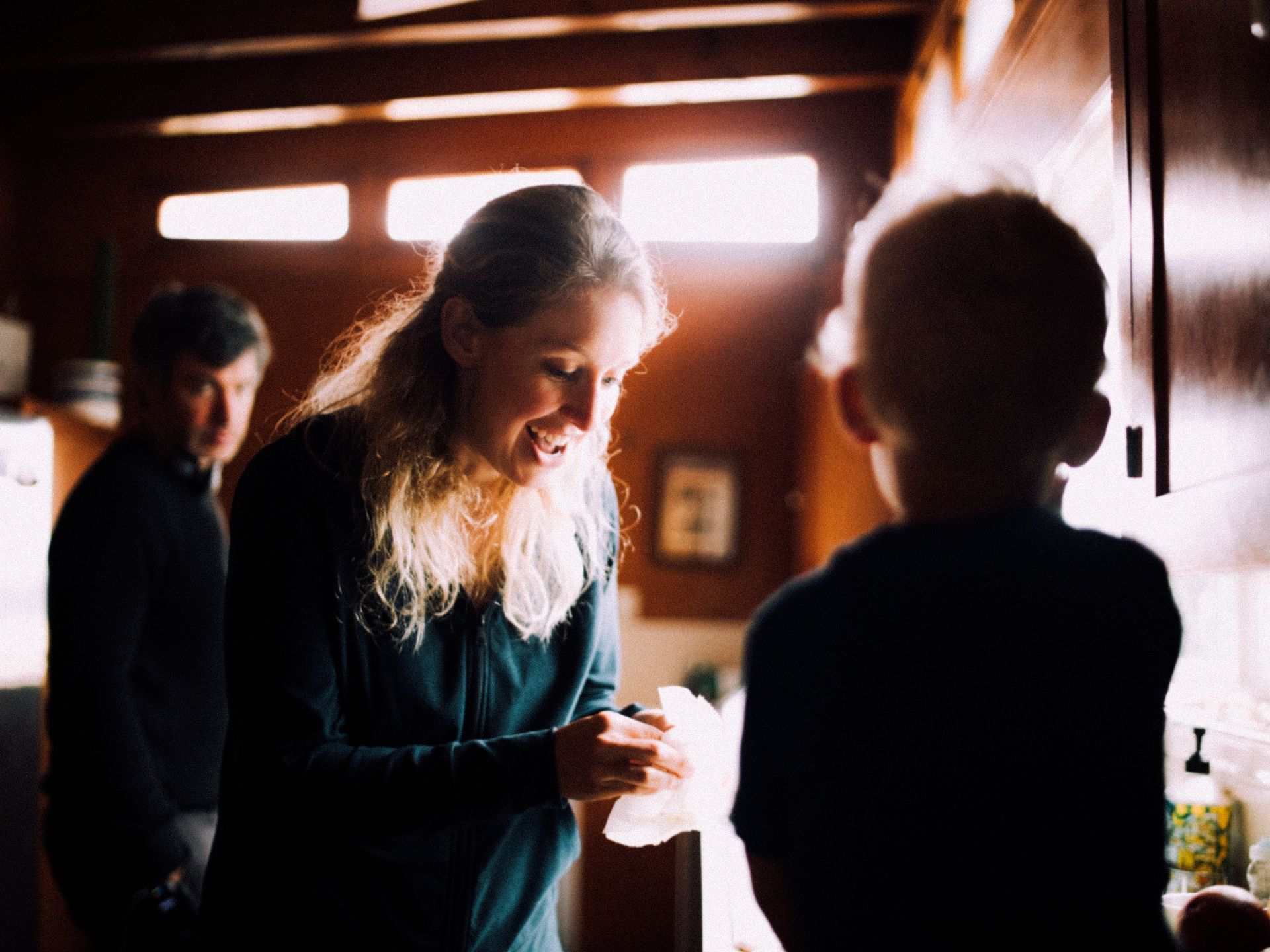 Elizabeth Holmes smiles while leaning toward a young child in a warmly lit kitchen in a still from the documentary you can see everything