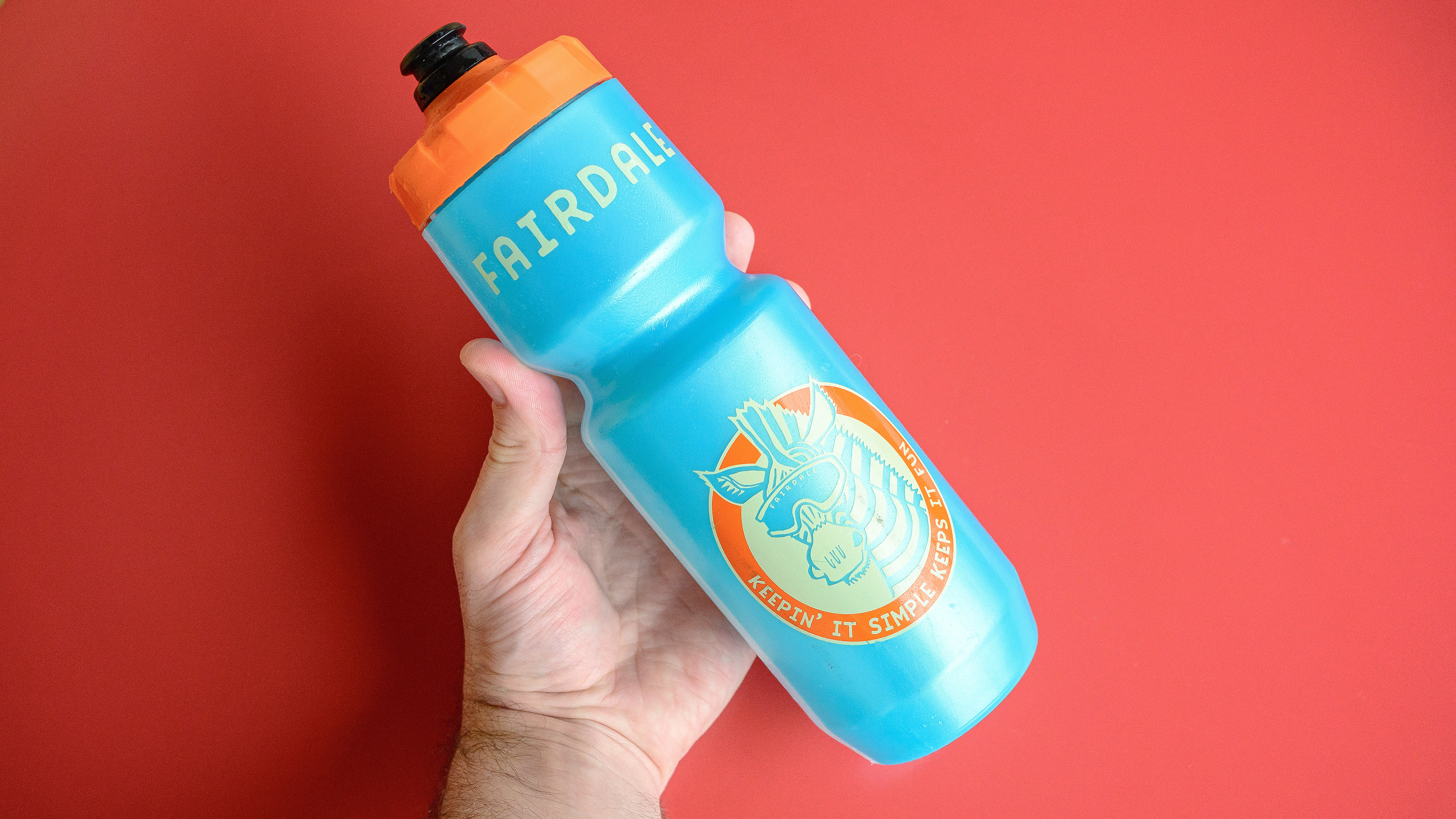 A blue bike water bottle in someone's hand on a red background.