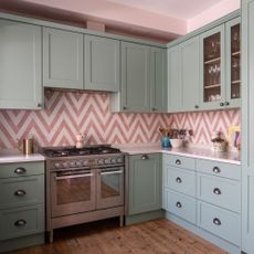 Green kitchen units with white and pink tile splashback in a zig-zag design
