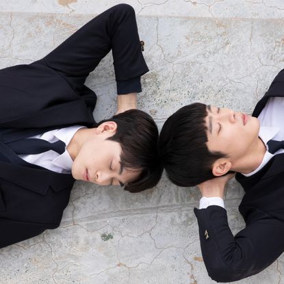 two young men lay on the ground resting their head in their hands in a still from the bl kdrama where your eyes linger