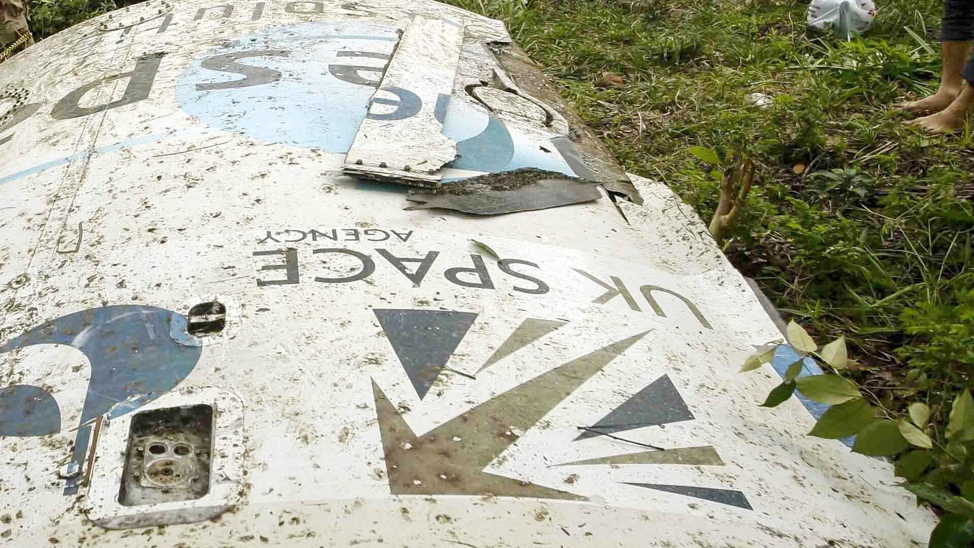 A white metal piece of space debris lies on a grassy lawn with the words "UK Space" upside down with the logo. 