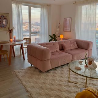 Pink velvet couch in airy living room with wooden floors and round glass-top coffee table