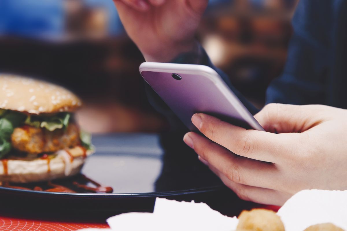 Somebody checking their phone next to a burger