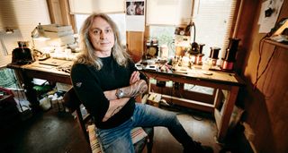 Tim Mills of Bare Knuckle pickups sits with his arms folded in his workshop/office.