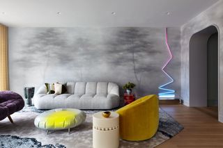 Living room with grey nature scene mural, grey sofa, yellow armchair, neon zig-zag wall light and neon and grey footrest