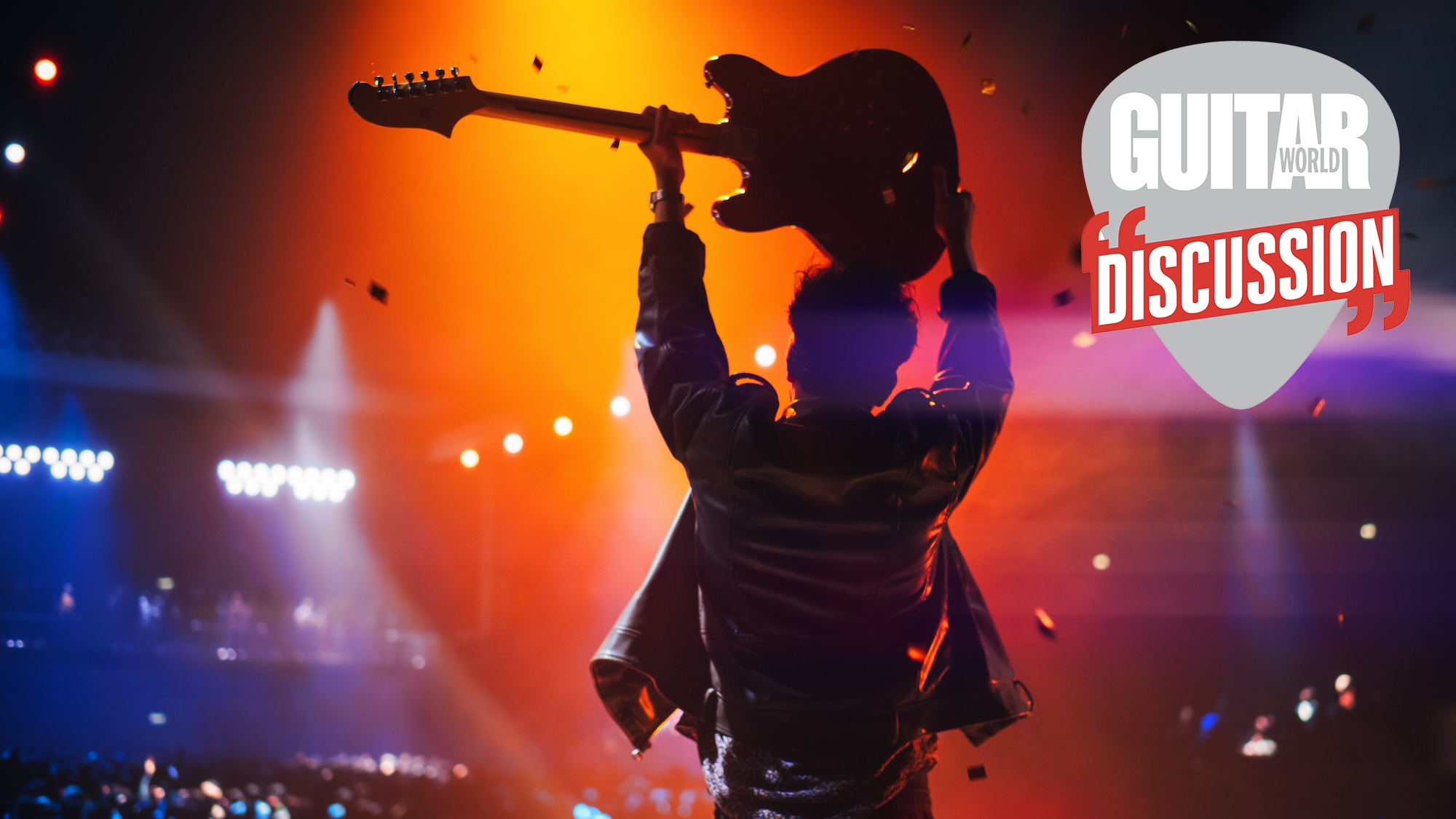 A guitarist, pictured in shadow from behind, holds their guitar aloft in front of a crowd 