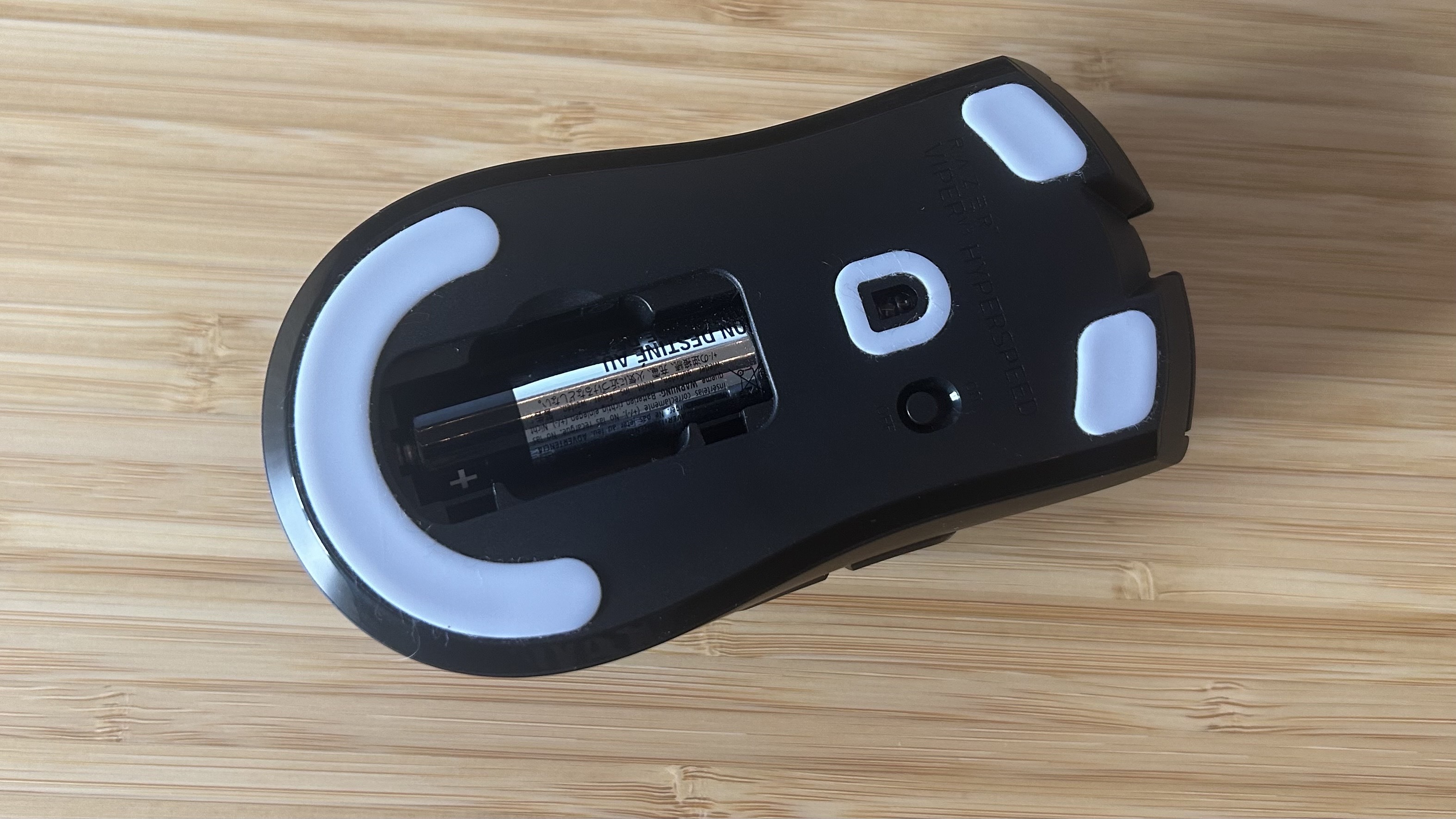 Razer Viper V3 Hyperspeed underside showing battery compartment and sensor on a wooden desk