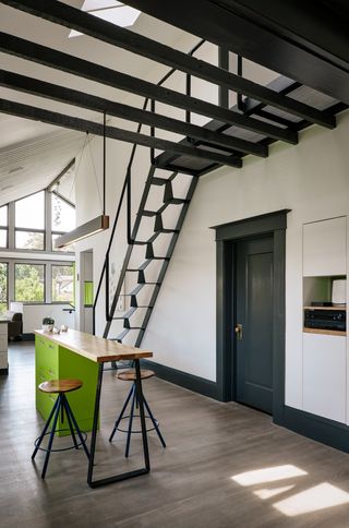 Green kitchen island with bar stools underneath a staircase at Alameda Renovation