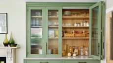 pale green kitchen pantry cupboard with reeded glass cabinet doors filled with jars and wooden crates