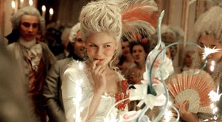 kirsten dunst in maire antoinette wearing a wig and white gown while eating a macaroon