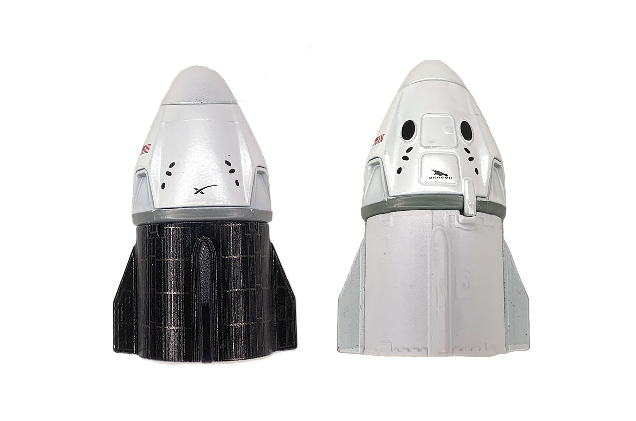 View of two Matchbox models of SpaceX Dragon crew capsules.