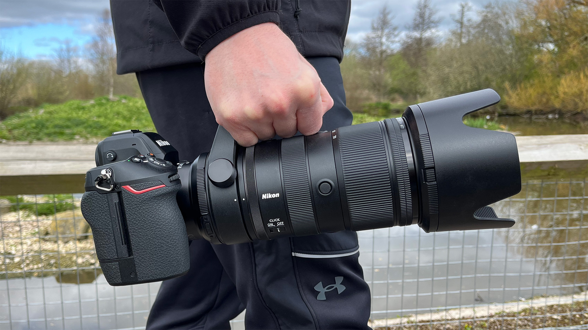Mike Harris holding Nikon Z 70-200mm f/2.8 VR S II by a lake with vegetation and trees in the background