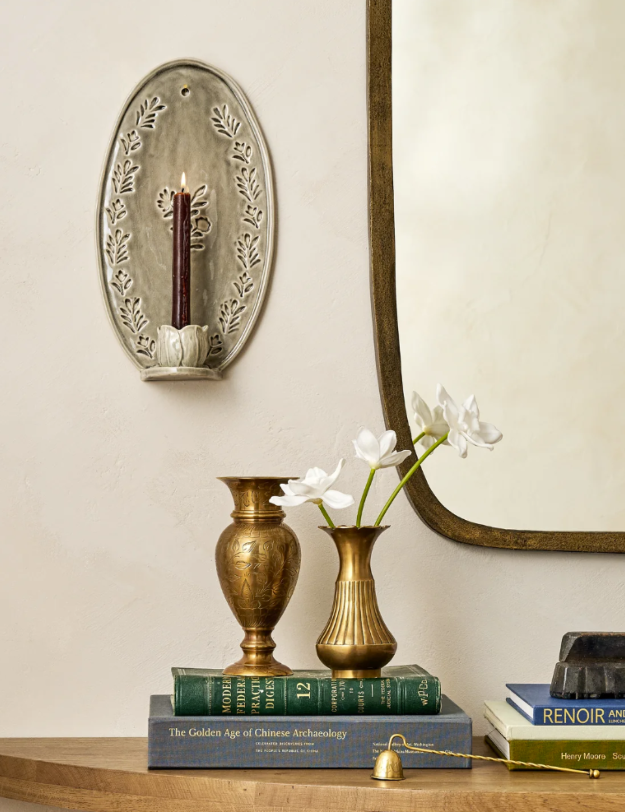 Close up console table vignette featuring a candle sconce, brass vase duo, and stacks of books