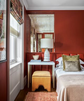 A bedroom with red walls, white ceilings and a yellow velvet stool