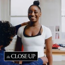 Simone Biles wears a t-shirt and sports bra while being fitted for a dress with Zac Posen