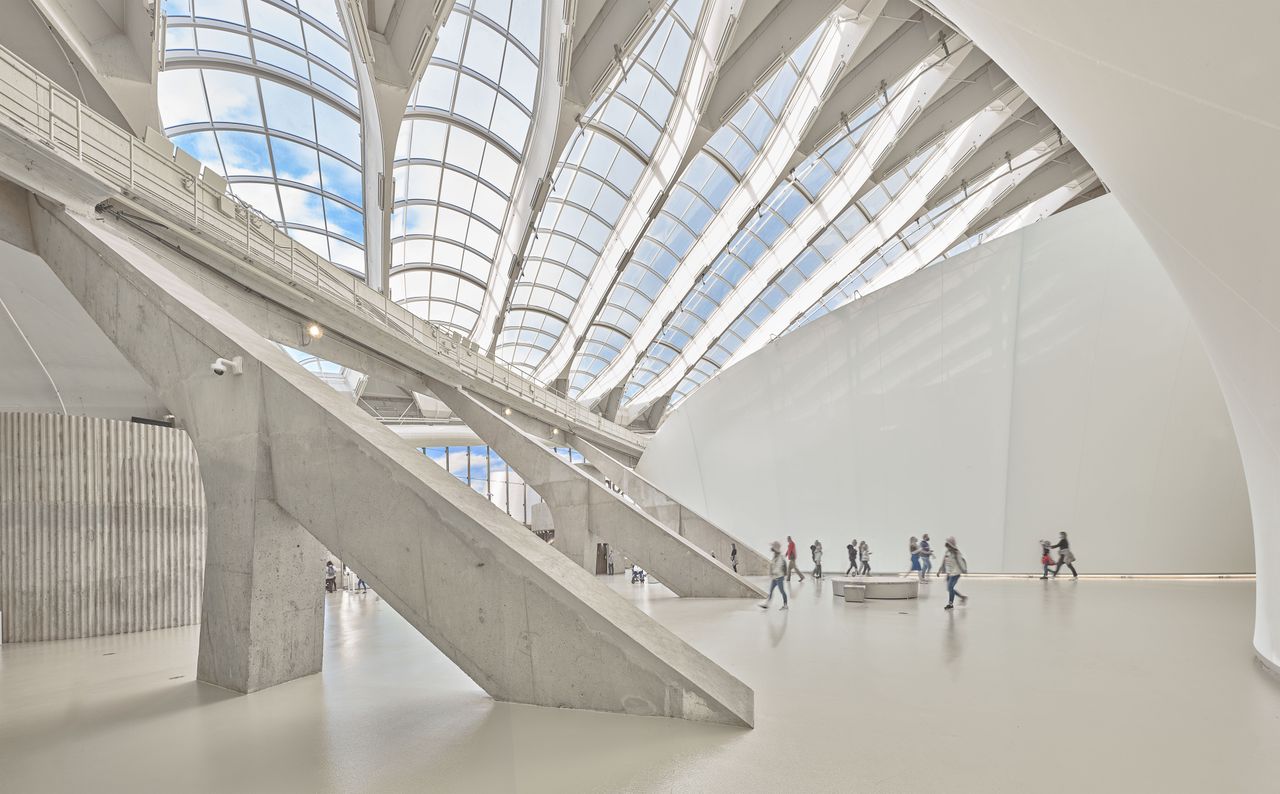 Montreal Biodome&#039;s white and grey stone design interior with glass ceiling arched framed windows on a sunny day, with people walking around inside the building