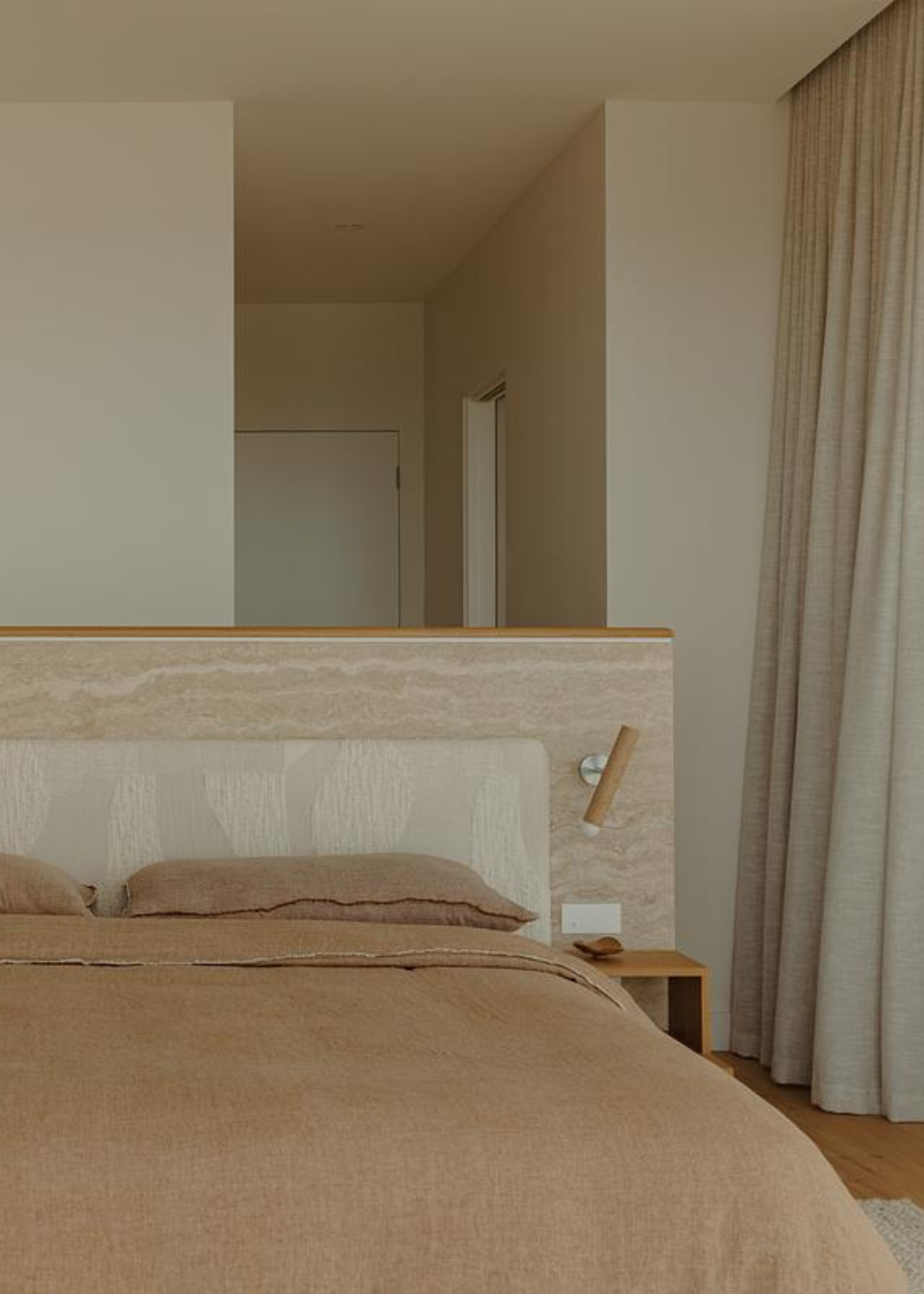 A cream bedroom with a stone bed wall, a patterned headboard and attached bedside sconces