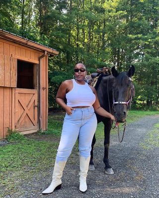 @aniyahmorinia wearing light blue skinny jeans, cowboy boots and a white racer tank top