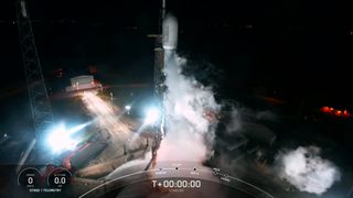 A black-and-white SpaceX rocket launches at night.
