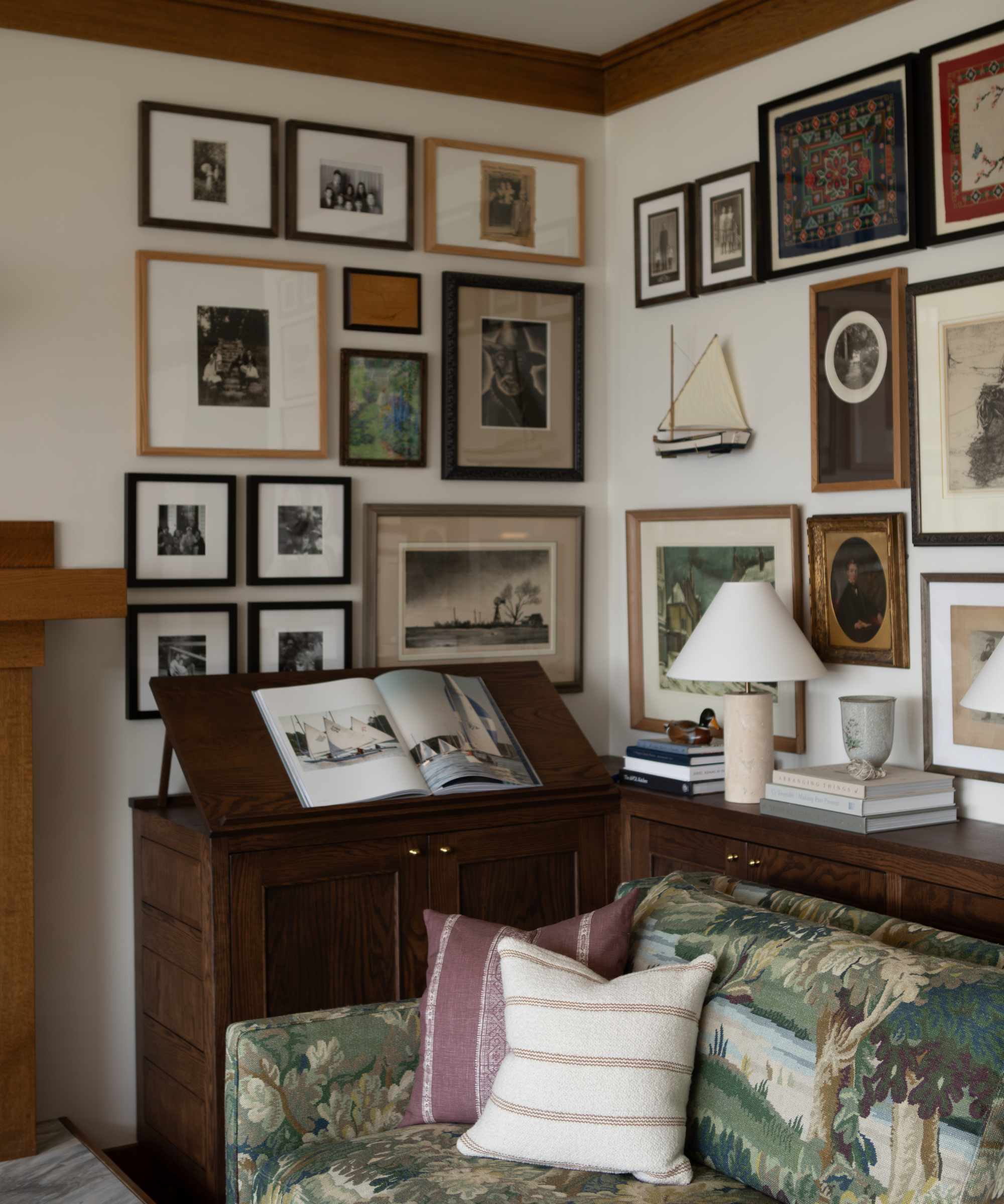 a room with lots of art hanging on the wall in the corner, a couch with a large green print, and accent pillows