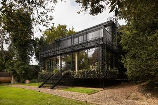 A black metal lattice house surrounded by woodlands