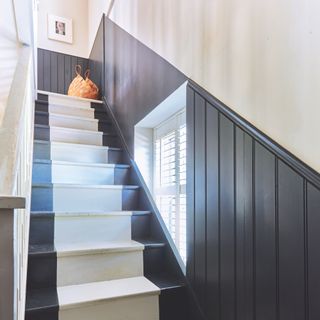 painted wooden staircase with dark grey edges and white painted runner, grey panelling on wall