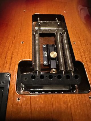 A photo of an Engl Hardtailer. The device allows a guitarist to block a floating tremolo unit when desired by pushing the Hardtailer into position and preventing the tremolo unit from moving. When engaged, as seen here installed on a Ernie Ball Music Man Cutlass, it prevents a “floating” trem block from pulling sharp, allowing you detune or change one or more strings without the other strings going out of tune.