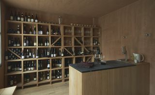 Wine room with wooden display case full of wine bottles and glasses and slate covered counter with tap and jug