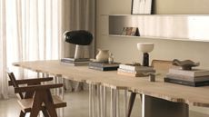 close up of stone dining table with textured edge, cream wall with stainless steel shelving, and armchair. the table is stacked with coffee table books with lamp