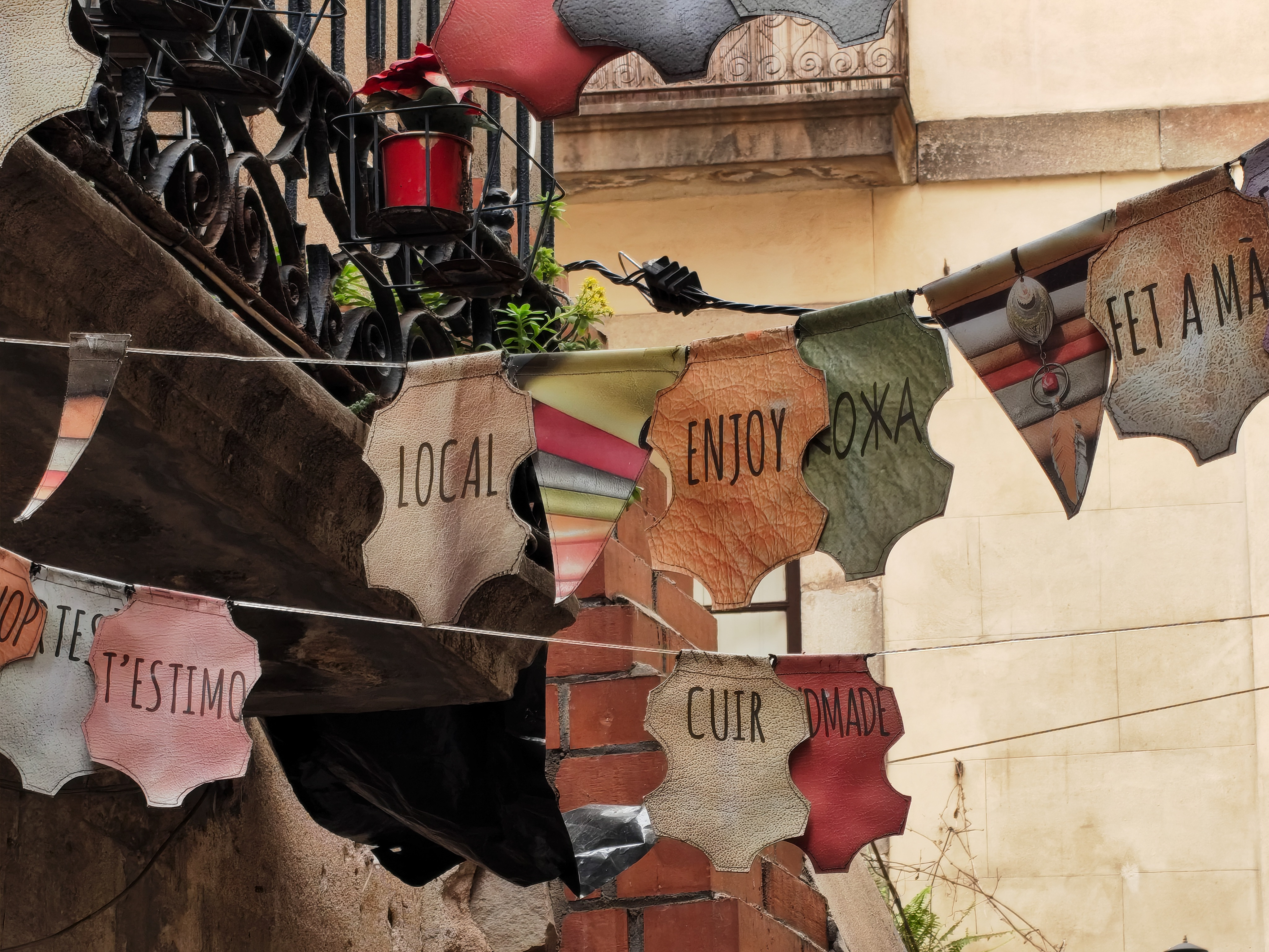 Decorative leather-shaped banner signs reading &ldquo;Local&rdquo;, &ldquo;Enjoy&rdquo;, and other words strung across a street market stall, photographed with the Nothing Phone (4a).