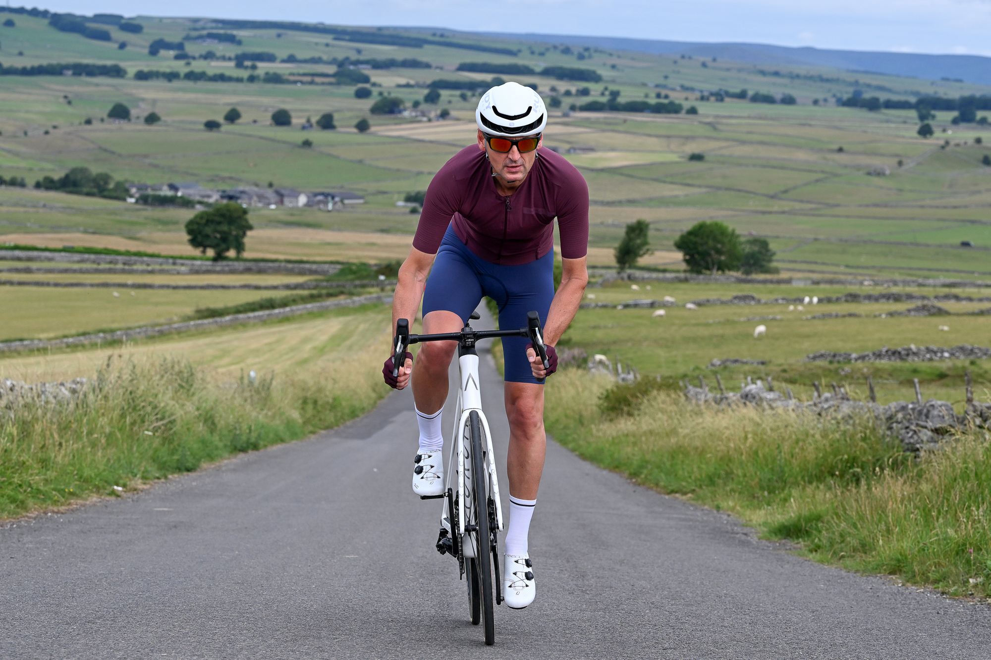 man wearing a white helmet and purple jersey riding at the camera up a hill