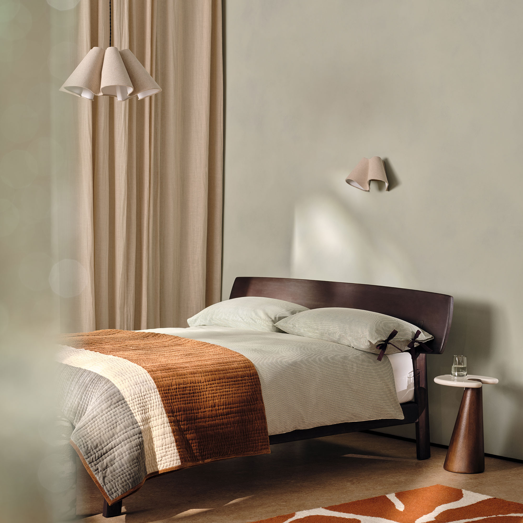 Dark wood double bed in a soft green room with rust accents and a pedestal bedside table