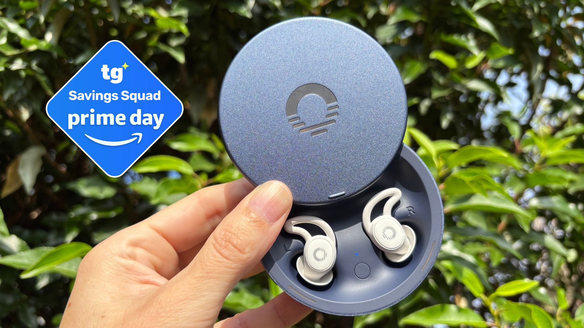 The image shows a woman's hand holding a pair of white earbuds in their navy blue case in front of a green plant. Inset to the left, a deal badge reads 'Tom's Guide Saving Squad Prime Day' 