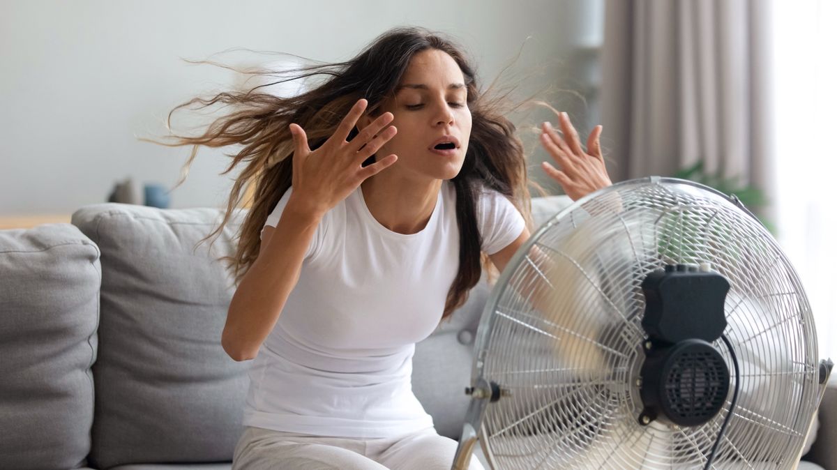 Woman suffering from heat at home sitting in front of fan 