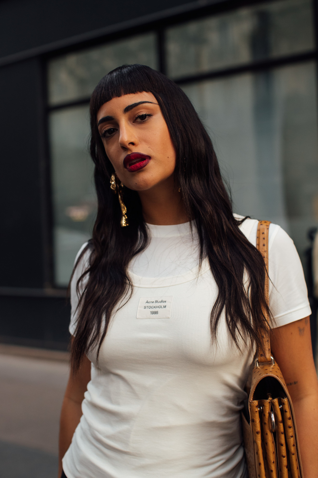 a woman with dark brown hair, red lipstick, and a white t-shirt looking at the camera