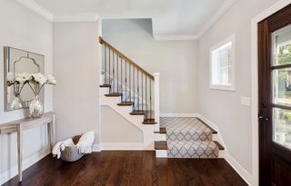 white hallway with dark wooden floor and stairs with stair runner and console table with mirror