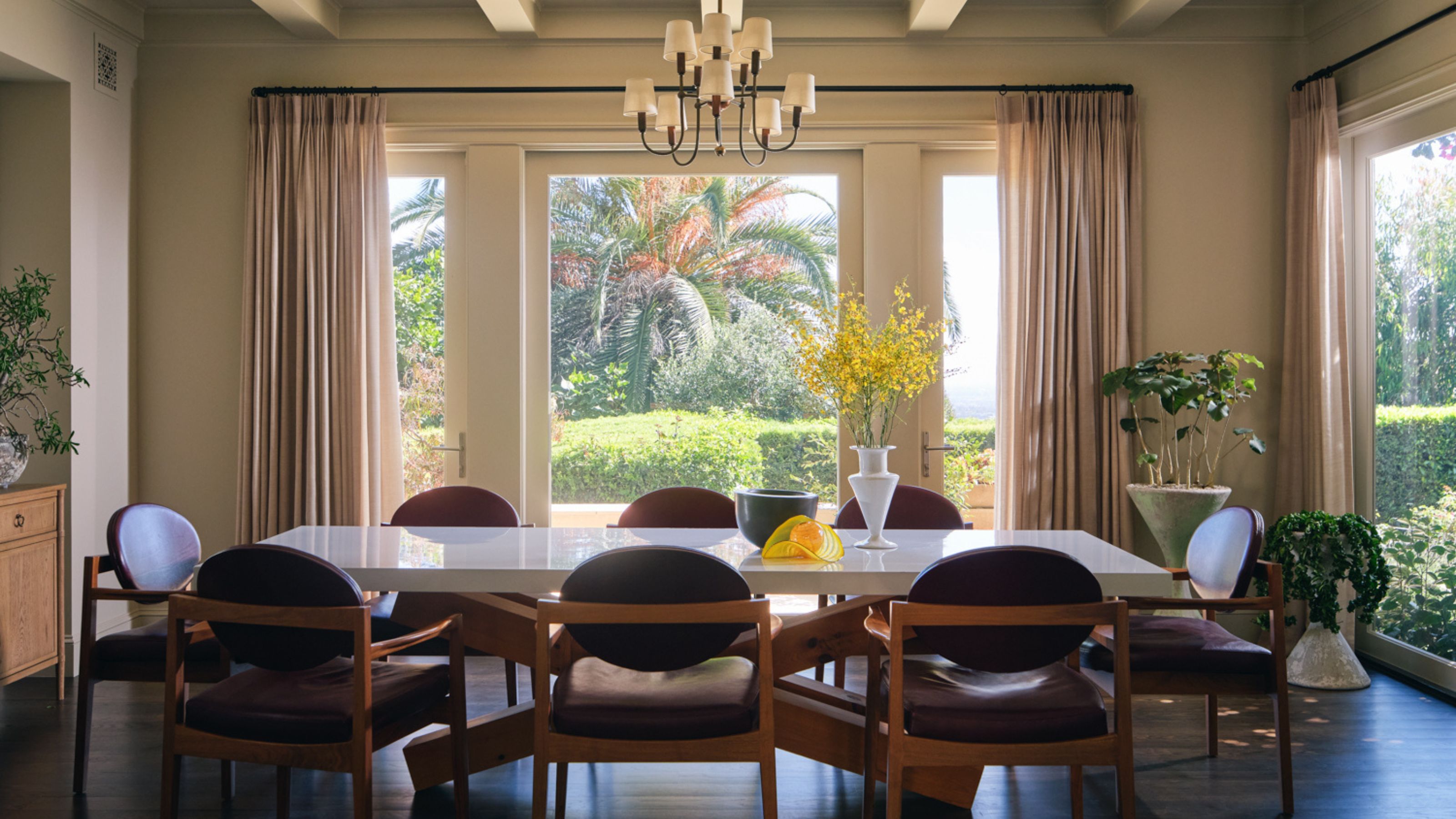 a large open dining room with ceiling beams and doors out to the garden with a large table and vintage leather and wooden chairs