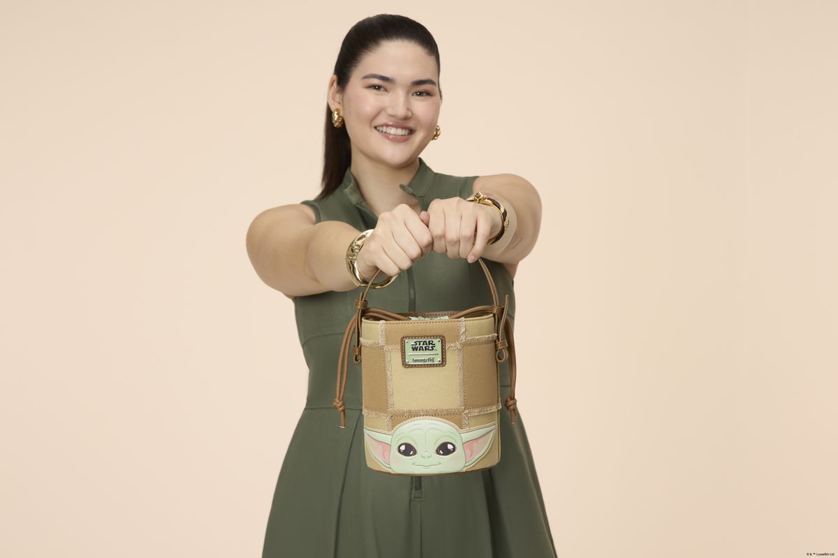 A woman holding a Loungefly bucket crossbody bag in a pink environment