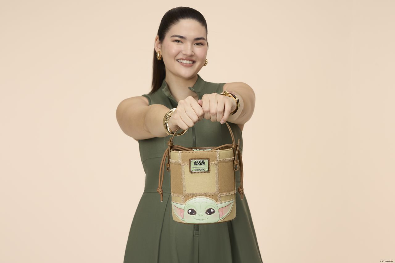 A woman holding a Loungefly bucket crossbody bag in a pink environment