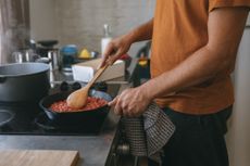 Man stirring pan of tomato sauce on stove with a wooden spoon